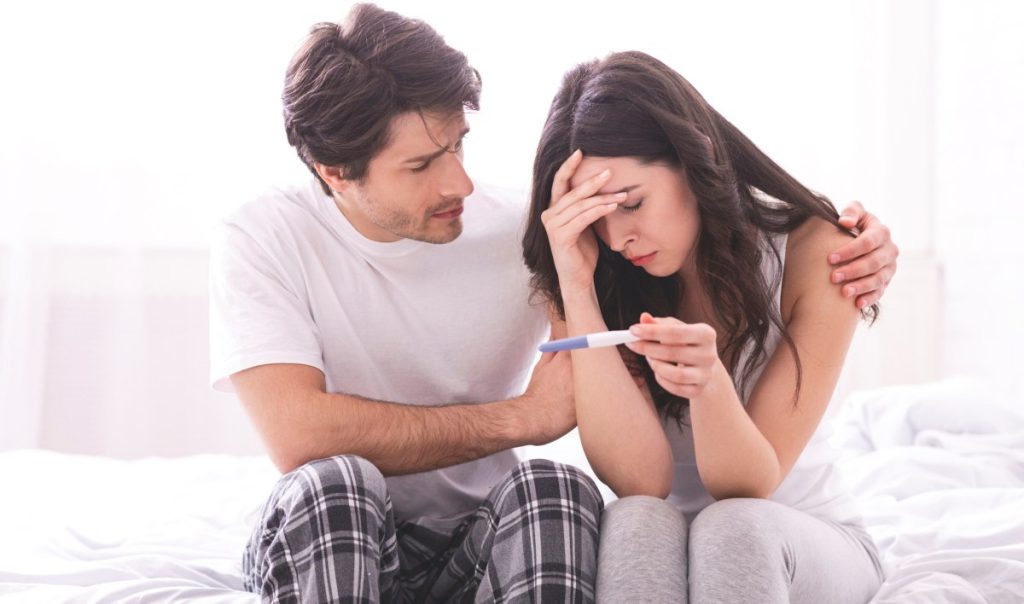Upset man comforting his depressed wife with negative pregnancy test,