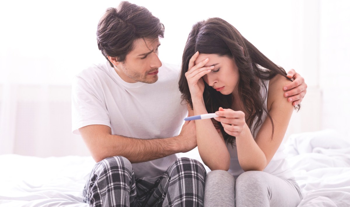 Upset man comforting his depressed wife with negative pregnancy test,