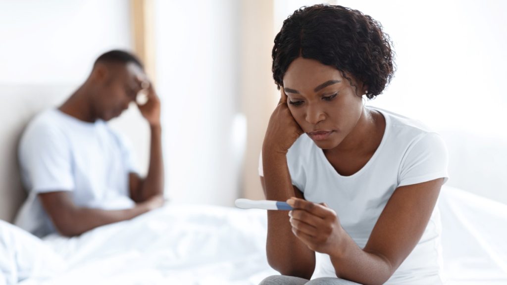 woman sitting on bed with sad look on her face while looking at a pregnancy test