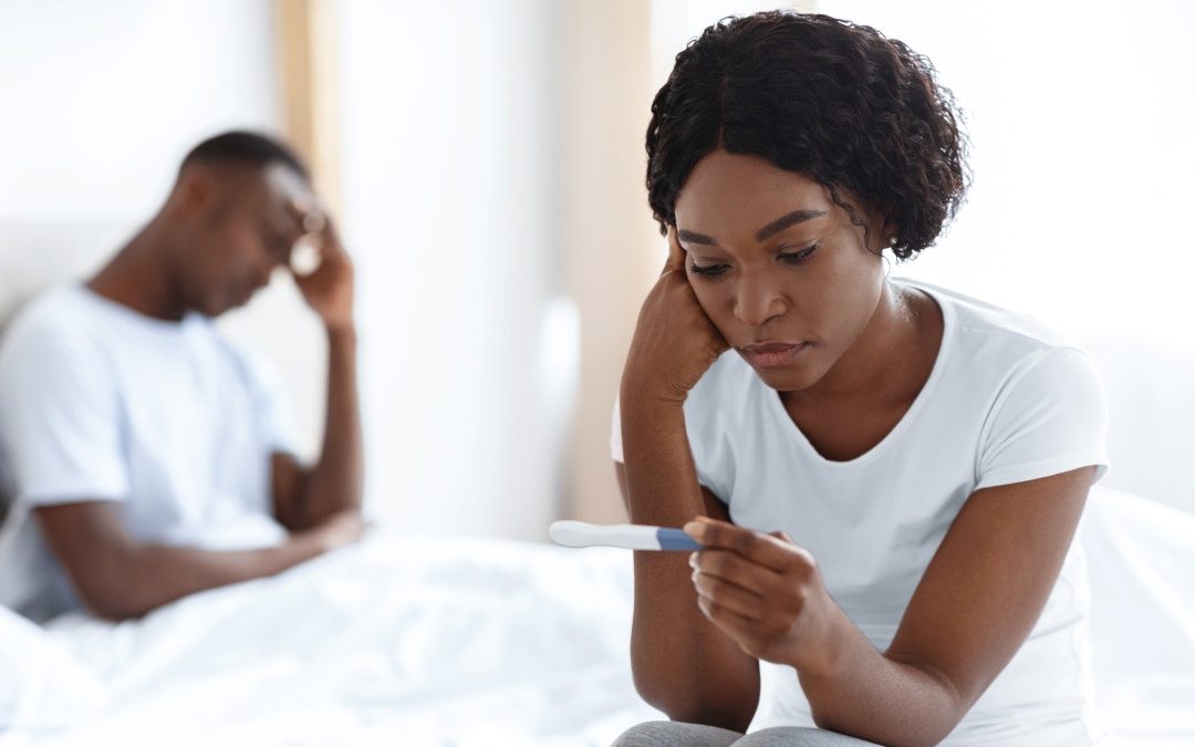 woman sitting on bed with sad look on her face while looking at a pregnancy test