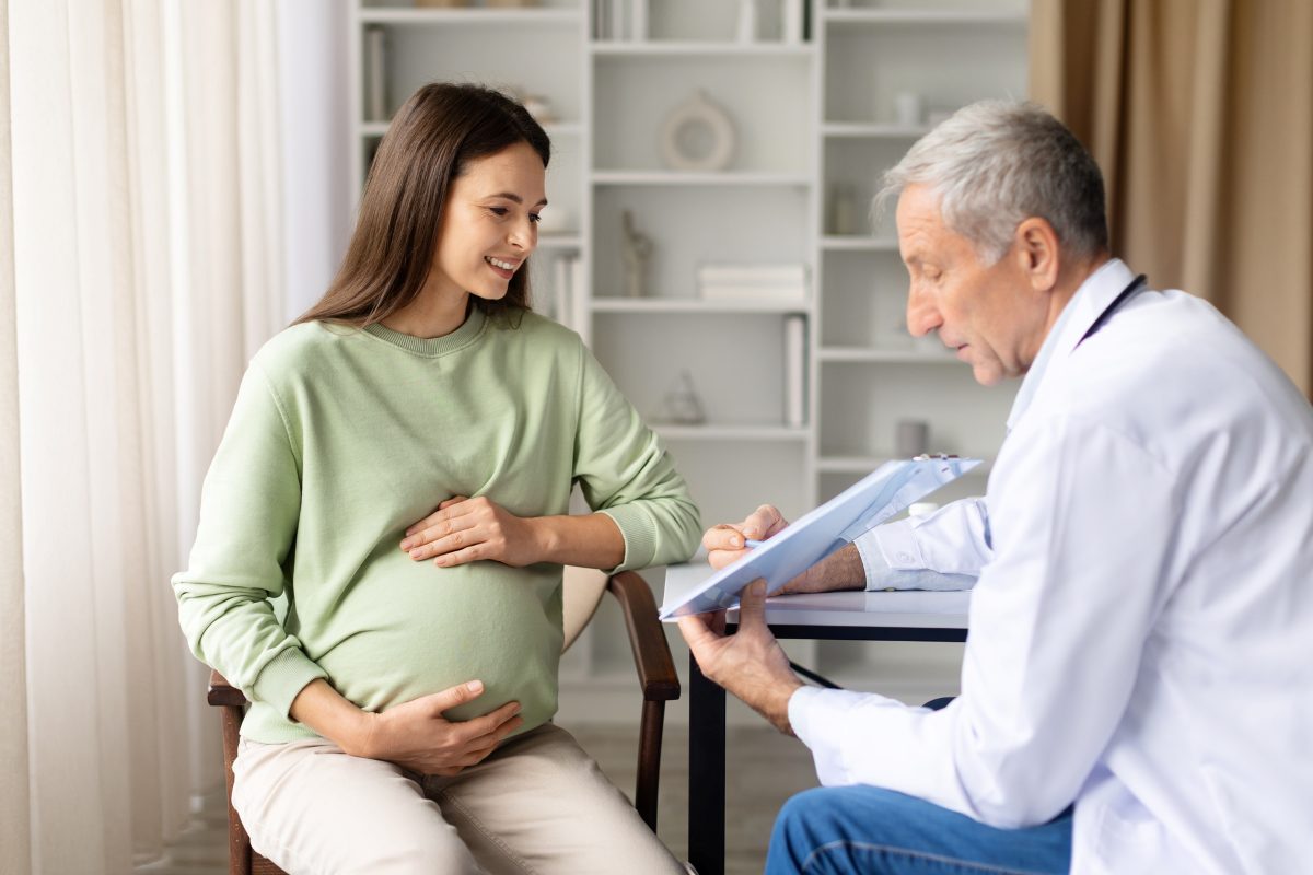 Smiling pregnant woman talking with senior male doctor in clinic during consultation