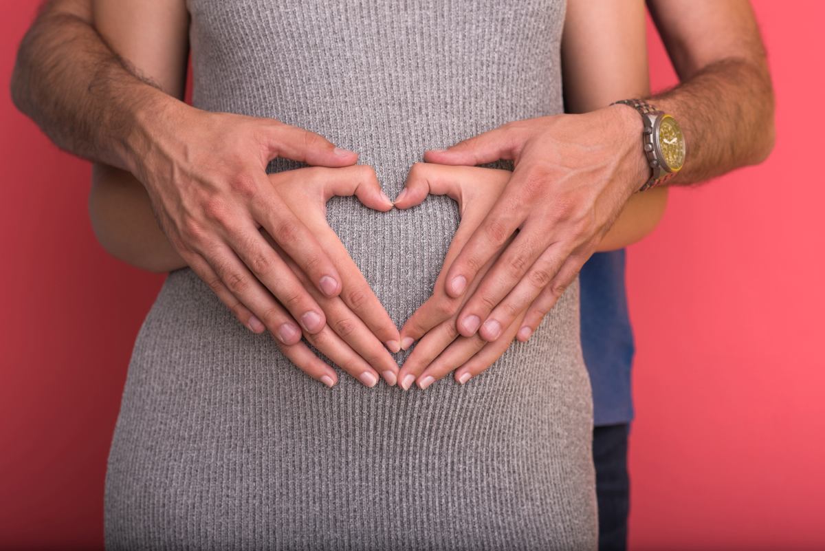 pregnant couple showing heart with their hands