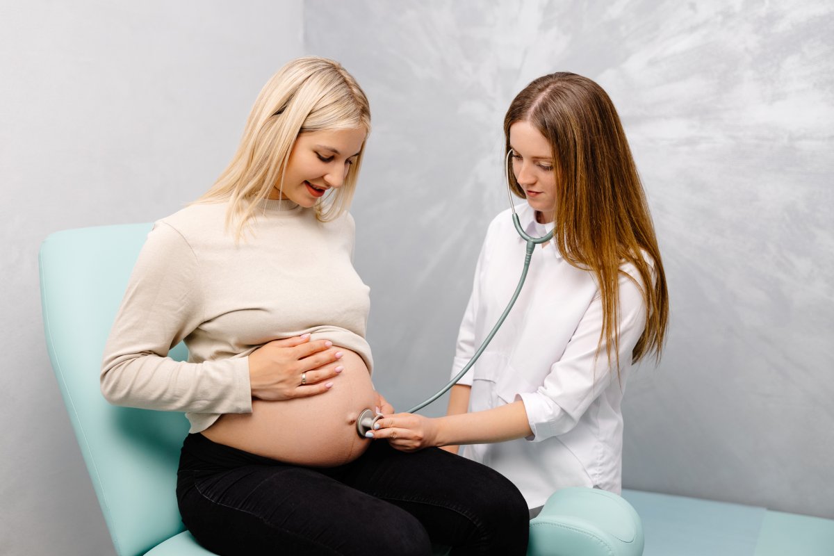 Female doctor using stethoscope examining pregnant woman in clinic