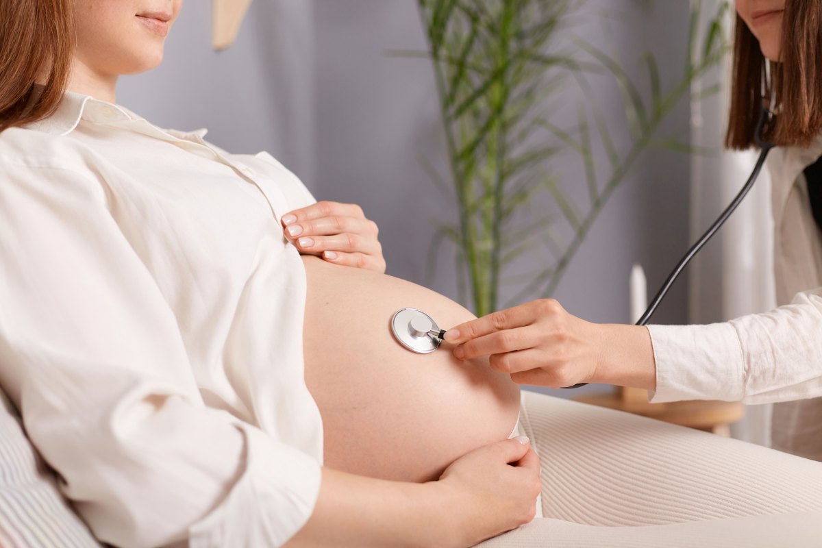 Amniotic Fluid Assessment Explained Unrecognizable pregnant female with bare belly and stethoscope doctor listening to baby heartbeat