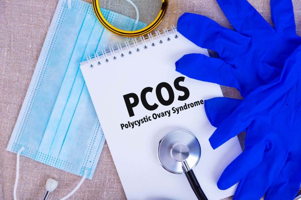 PCOS Polycystic Ovary Syndrome, the text is written on a notepad, a disposable medical mask, medical gloves, a stethoscope on a linen background