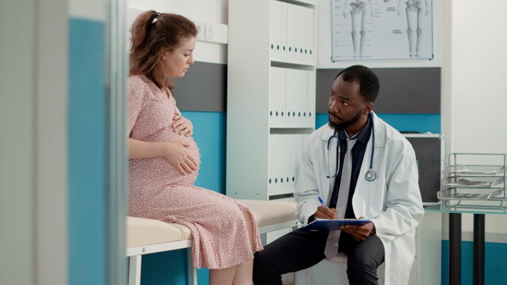 General practitioner attending consultation and taking notes to give prescription medicine to patient expecting child in office