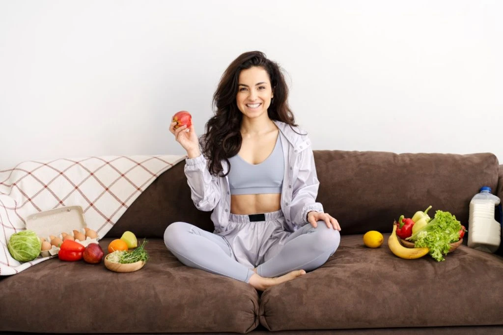 beautiful woman holding apple surrounded by healthy food on sofa